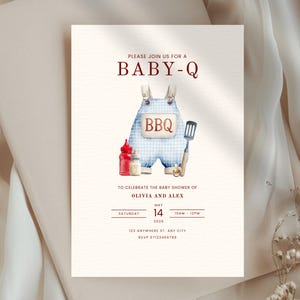 May include: Baby shower invitation with a watercolor design. The invitation features the text "BABY-Q" in red, along with an illustration of blue overalls with the word "BBQ". Includes details for Olivia and Alex's baby shower, date, time, and RSVP information.