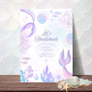 May include: A mermaid-themed invitation with the text "Let's Shellabrate" in elegant script. The design features watercolor illustrations of mermaid tails, coral, and fish in shades of purple, blue, and pink. The invitation is for Olivia's 2nd birthday.