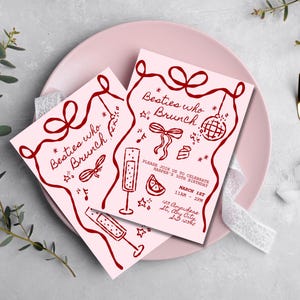 May include: Two pink invitation cards with burgundy text and illustrations, reading "Besties who Brunch." The cards feature a bow, disco ball, champagne flutes, and a slice of citrus. The invitations are on a pink plate with gold cutlery.