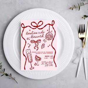 May include: A pink invitation card with the text "Besties who Brunch" and event details in dark red. The card features illustrations of a disco ball, champagne flute, and cake. The invitation is placed on a white plate with a fork and knife.