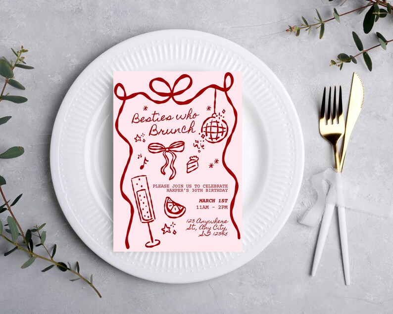 May include: A pink invitation card with the text "Besties who Brunch" and event details in dark red. The card features illustrations of a disco ball, champagne flute, and cake. The invitation is placed on a white plate with a fork and knife.