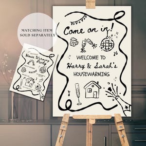 May include: A cream-colored housewarming party sign on a wooden easel. The sign reads "Come on in! Welcome to Harry & Sarah's Housewarming" with decorative illustrations. A smaller matching card is also visible.