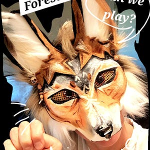 hi! this is friendly Forest. Forest is a therian coyote mask with a playful spirit. He is adorable and just the sight of him will warm your heart. If you would love a mask that is also your best friend look no further than Forest. He has large eyes that look both intense and friendly at the same time. He has patterns on his face like lines in wood, painted in a cheery salmon color, contrasted with a bluish gray. His ears are engulfed in bark like tufts. See him on my Tiktok and IG