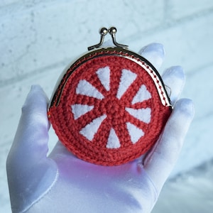 May include: A red crocheted coin purse with a white crocheted flower design. The purse has a silver metal clasp.