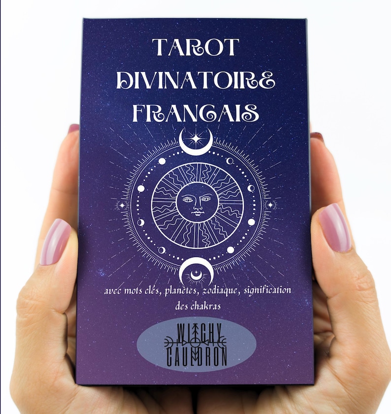 May include: A tarot card deck with a dark blue cover featuring white text that reads "TAROT DIVINATOIRE FRANGAIS". The design includes a sun, crescent moons, and a circular pattern. The bottom of the deck has the text "WITCHY CAUMORON".