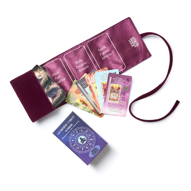 May include: A tarot card set with a deep purple card holder and a matching box. The card holder is open, revealing several tarot cards with diverse illustrations and text. The box reads "LEARNING TAROT CARDS".