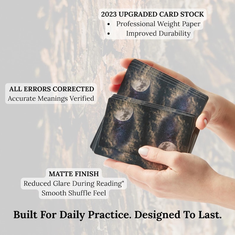 May include: A deck of tarot cards with a matte finish, featuring a celestial design with a moon and stars. The cards are held in a person's hands. Text on the cards reads "2023 Upgraded Card Stock" and "Built For Daily Practice. Designed To Last."