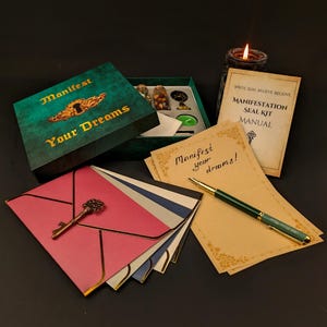 May include: A manifestation seal kit with a green and gold box that reads "Manifest Your Dreams." The kit includes a manual, stationery, a pen, and a key-shaped charm. The kit also contains small jars and a candle.