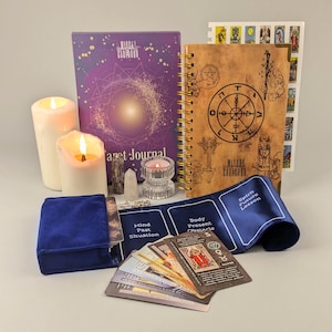 May include: A collection of spiritual items including a tarot journal, a spiral-bound notebook, tarot cards, a blue velvet card holder, candles, and crystals. The journal is purple with gold accents and the notebook is brown with gold spiral binding. The cards have various illustrations.
