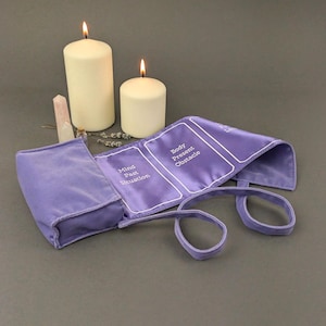May include: A purple velvet pouch with a strap, open to reveal a set of tarot cards with the words "Mind Past Situation", "Body Present Obstacle" printed on them. Two white candles are in the background.