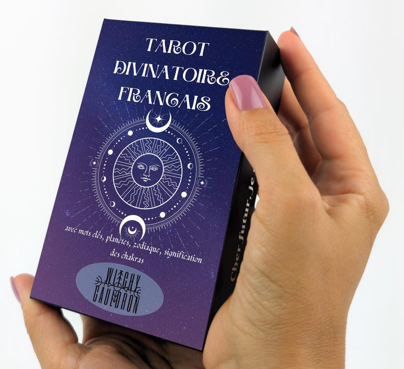 May include: A tarot card deck with a dark blue and purple gradient background. The deck features white text that reads "TAROT DIVINATOIRE FRANCAIS" and a circular design with a sun, moons, and stars. The text "WITCHY CAULDRON" is also visible.