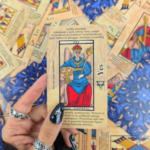 May include: The Empress tarot card, a depiction of a woman in a blue and red robe, sitting on a throne with a scepter and a crown. The card is surrounded by other tarot cards and has the text "Yes" and "Act on your instincts." printed on it.