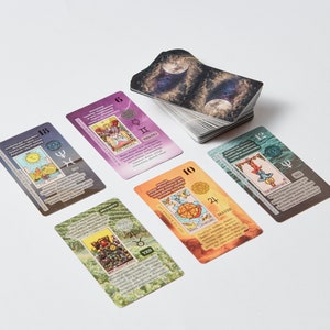 May include: A set of tarot cards with colorful illustrations and text. The cards are laid out on a white surface. The cards include the numbers 6, 10, 12, 18, and 24. The text on the cards includes "The Lovers", "The Hanged Man", "The Moon", "Wheel of Fortune", and "The Devil".