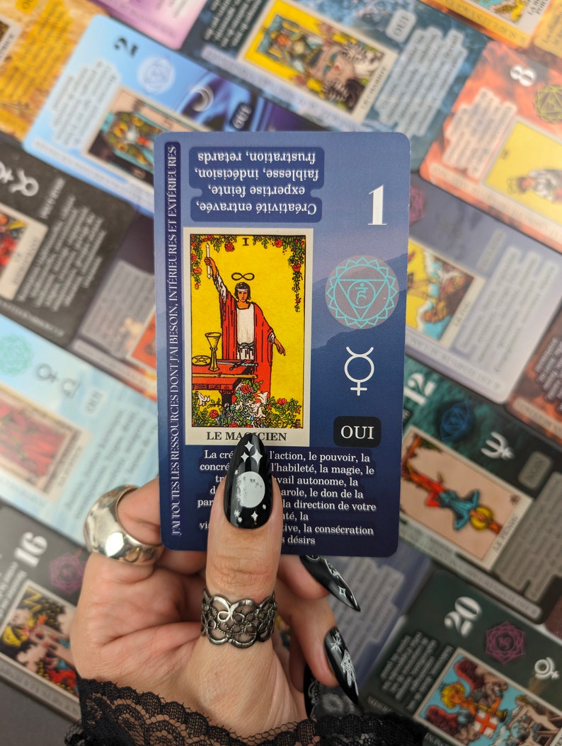 May include: A tarot card with the number 1, featuring an illustration of a figure with a wand. The card has text in French, including "Le Magicien" and "Oui." Other tarot cards are visible in the background.