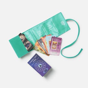 May include: A teal tarot card holder with a matching ribbon, holding a deck of tarot cards. The holder has labeled sections for Mind, Body, Spirit, and Future. A small purple box of "Learning Tarot Cards" is also visible.