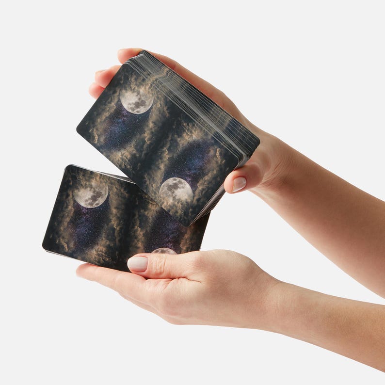 May include: A deck of cards with a moon and stars design. The cards are being held in a person's hands.