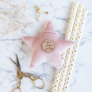 May include: A pink velvet star-shaped pillow with a wooden circle tag that says "your project or logo". The pillow is surrounded by gold and white striped straws and gold scissors.