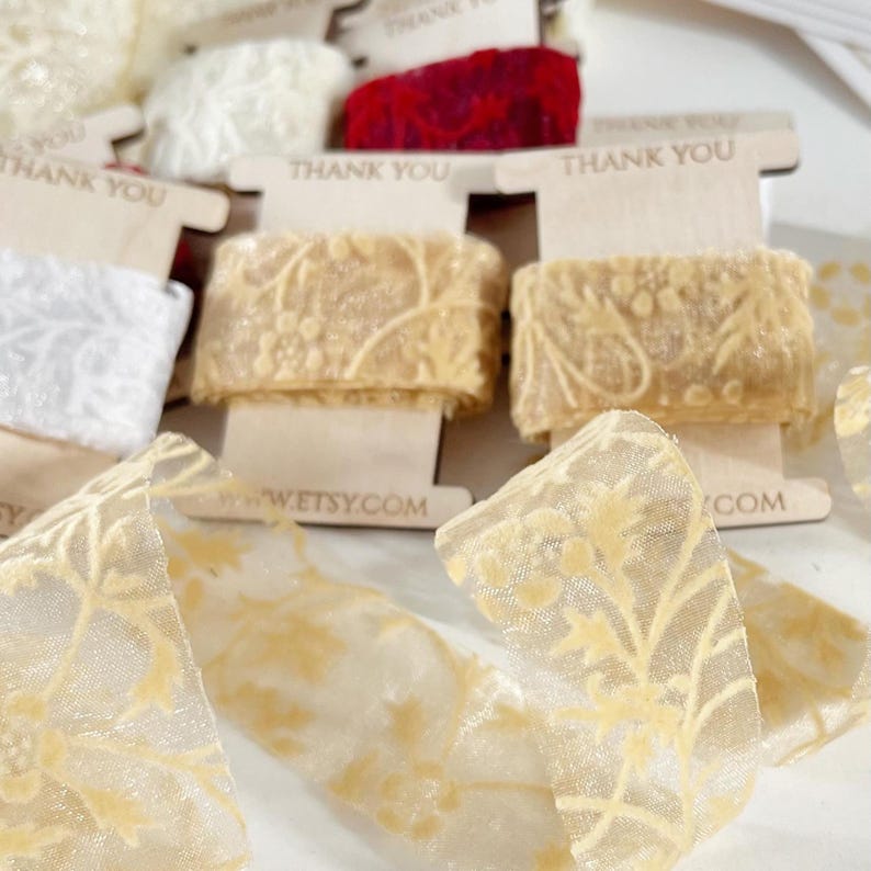 Light golden lace ribbon with delicate velvet floral design, ideal for wedding decor, elegant packaging, or DIY crafts. The semi-sheer texture adds a soft, romantic touch, and the ribbon is neatly wrapped on a wooden spool for presentation and storage.