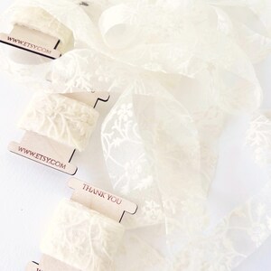 Creamy floral lace ribbon delicately wrapped on wooden spools, ready for your creative projects. Perfect for decorating wedding invitations, place cards, menus, and gift packaging with a soft, romantic touch. Adds charm and elegance to every detail.