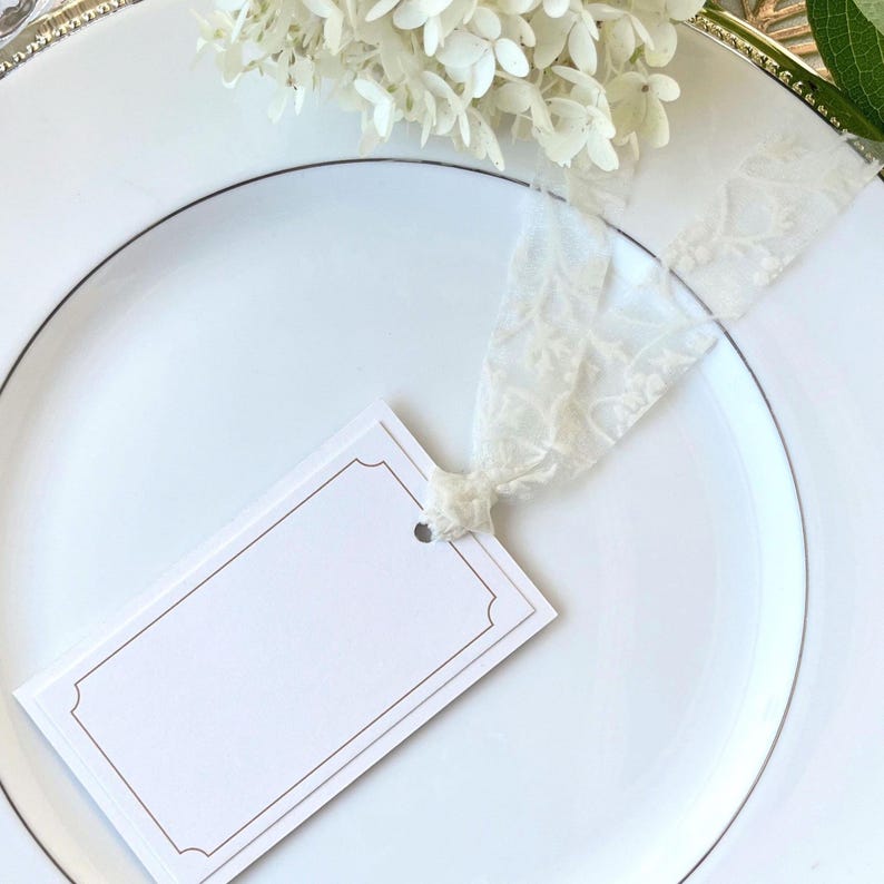 Elegant white lace ribbon tied to a minimalist tag card, perfect for wedding table settings, guest name cards, or thoughtful gift wrapping. The sheer floral texture adds a refined, romantic detail ideal for formal celebrations and elegant events.
