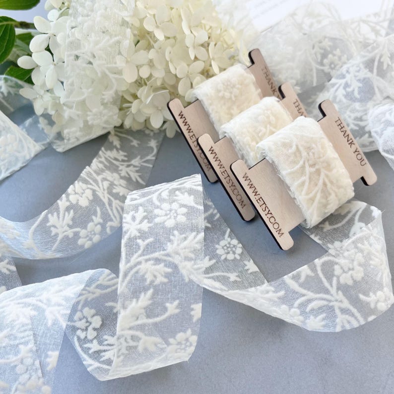 Delicate flower flocked lace ribbon in elegant ivory tones, perfect for wedding invitations, gift wrapping, card making, and special packaging. The intricate floral pattern adds a luxurious, romantic finish to any creative project or celebration.