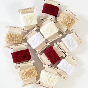 A variety of delicate lace ribbons in elegant shades of white, gold, and burgundy, neatly wrapped on branded spools. Ideal for creative gift wrapping, wedding stationery, craft projects, or luxury product packaging with a romantic, textured touch.