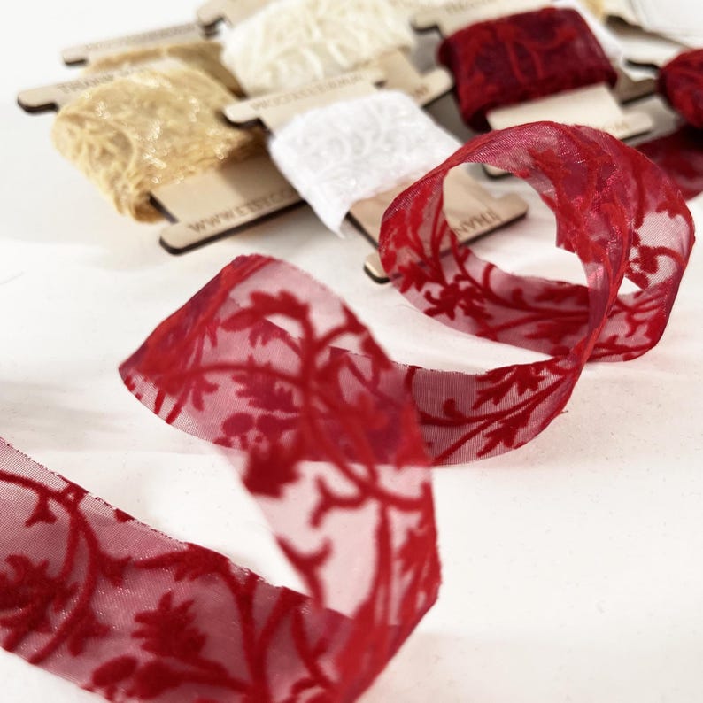 Deep red lace ribbon featuring intricate velvet floral patterns, perfect for romantic or festive designs. Adds elegance to wedding invitations, holiday packaging, or handmade cards. Presented on a wooden spool for easy use and stylish display.