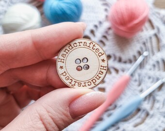 May include: A wooden button with the word "handcrafted" written around the edge. The button has four holes and is a light brown color.