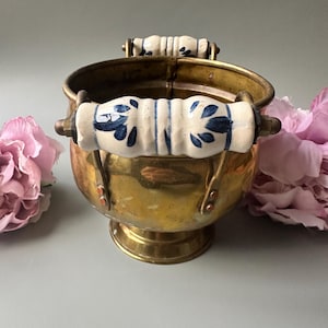 Può includere: Un secchio vintage in ottone con due manici in ceramica bianca decorati con motivi floreali blu. Il secchio ha un corpo arrotondato e una piccola base a piedistallo. Le maniglie sono fissate con hardware in ottone.