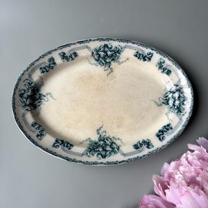 Könnte beinhalten: Ovale Servierplatte mit cremefarbenem Mittelteil und teal-farbenem Blumendesign am Rand. Die Platte hat einen dekorativen Rand und ist wahrscheinlich Vintage oder antik. Das Blumenmuster wiederholt sich am Rand.