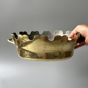 Op de afbeelding: Een ronde koperen kom met een geschulpte bovenrand en twee kleine handvatten aan de zijkanten. Het buitenoppervlak van de kom heeft een gepolijste metalen afwerking met zichtbare tekenen van natuurlijke patina en kleine onvolkomenheden.