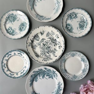 May include: A collection of six round ceramic plates arranged in a circular pattern, each featuring a white base with intricate teal blue floral and bird motifs. The plates have scalloped edges and varying decorative patterns, with one larger plate centred.