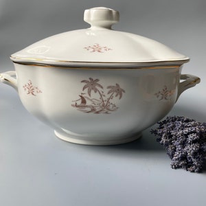 May include: White porcelain soup tureen with a lid and two handles. The tureen features a brown and gold design of palm trees and a sailboat.
