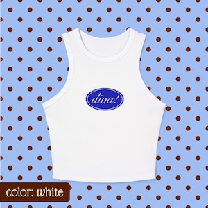 May include: A white sleeveless crop top featuring a centered blue oval graphic with the word diva! printed in white lowercase script. The garment has a high rounded neckline and wide shoulder straps, presenting a clean and simple design.