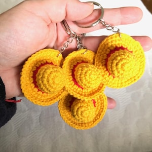 Peut inclure: Quatre porte-clés en crochet jaunes en forme de chapeau avec une bande rouge, attachés à un anneau en métal argenté. Les chapeaux sont faits de fil. Chaque porte-clés est une version miniature d'un chapeau.
