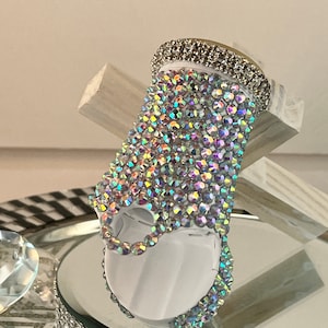 May include: A white ring holder with a clear iridescent crystal design. The holder is covered in crystals and has a silver band around the top.