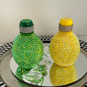 May include: Two decorative bottles covered in iridescent rhinestones. One bottle is green and the other is yellow.