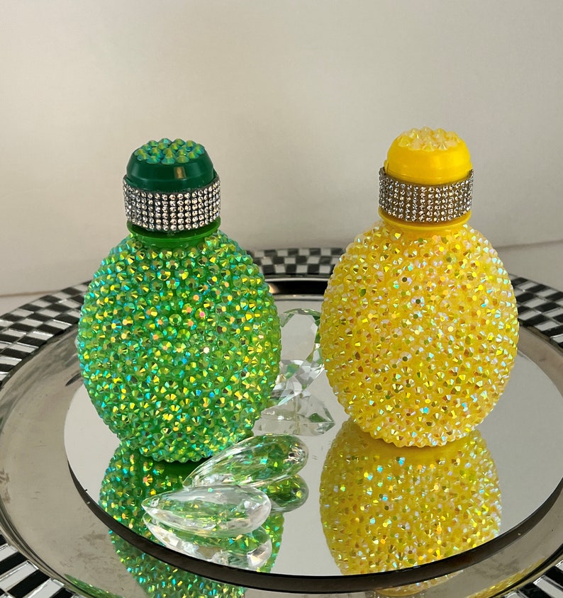 May include: Two decorative bottles covered in iridescent rhinestones. One bottle is green and the other is yellow.