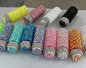 May include: Assortment of 14 small, cylindrical bottles covered in iridescent rhinestones. The bottles have silver caps and come in a variety of colors, including pink, blue, green, yellow, and orange.