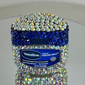 May include: A blue and white jar of Vaseline Healing Jelly with a clear lid. The jar is covered in iridescent rhinestones. The label reads "Vaseline. Original HEALING JELLY™ Dermatologist Recommended 100% White Petrolatum Skin Protectant NET WT 1.75 OZ (49g)"