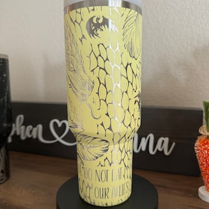 May include: A yellow stainless steel tumbler with a silver dragon design and the text "We do not eat our allies".