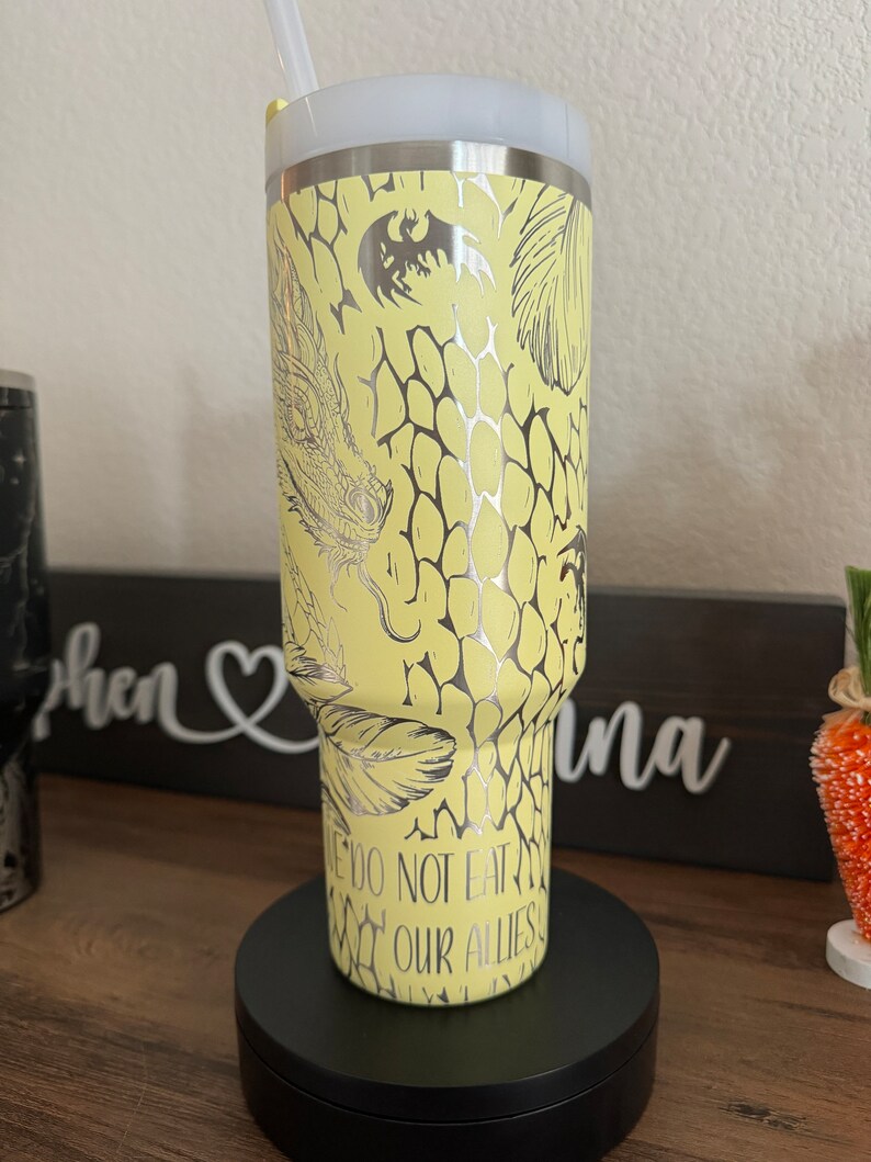 May include: A yellow stainless steel tumbler with a silver dragon design and the text "We do not eat our allies".