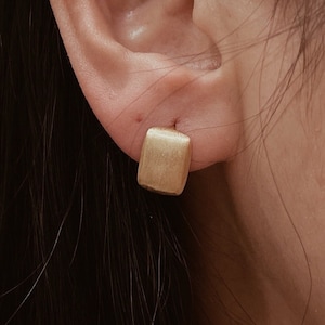 May include: A pair of gold square stud earrings. The earrings are simple and elegant, and would make a great gift for any occasion.