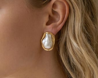 May include: An earring featuring an irregular, organic-shaped white pearl set within a textured, gold-toned metal frame. The piece has a polished finish and is secured to the earlobe. The text Ash Mollie Studio ESTD 2021 is visible at the bottom.
