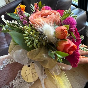 May include: A bridal bouquet with pink, orange, and white flowers, greenery, and a gold tag with the text "PCH. Hoco 2024".