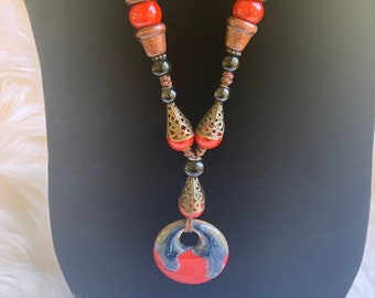 Cool toned ceramic necklace made with various shades, bead size and bronze ornate with eye catching pendant.