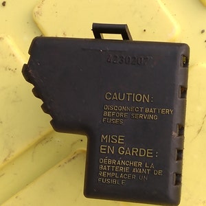 Peut inclure: Couvre-boîte à fusibles noir avec le texte "CAUTION: DISCONNECT BATTERY BEFORE SERVING FUSES" et "MISE EN GARDE: DÉBRANCHER LA BATTERIE AVANT DE REMPLACER UN FUSIBLE".