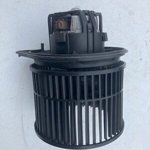 Puede incluir: Motor de ventilador de coche de plástico negro con una jaula de metal. El motor tiene una carcasa de plástico negro y una hélice de ventilador de metal.