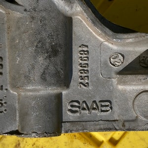 Peut inclure: Gros plan sur une pièce métallique grise avec le texte "SAAB" et le numéro "25896684" estampés dessus. La pièce porte également le texte "TCP 2. 769 HT" estampé dessus.