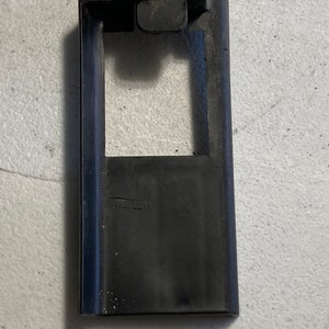 Puede incluir: Pomo de puerta de plástico negro con una abertura rectangular y una pequeña pestaña en la parte superior.